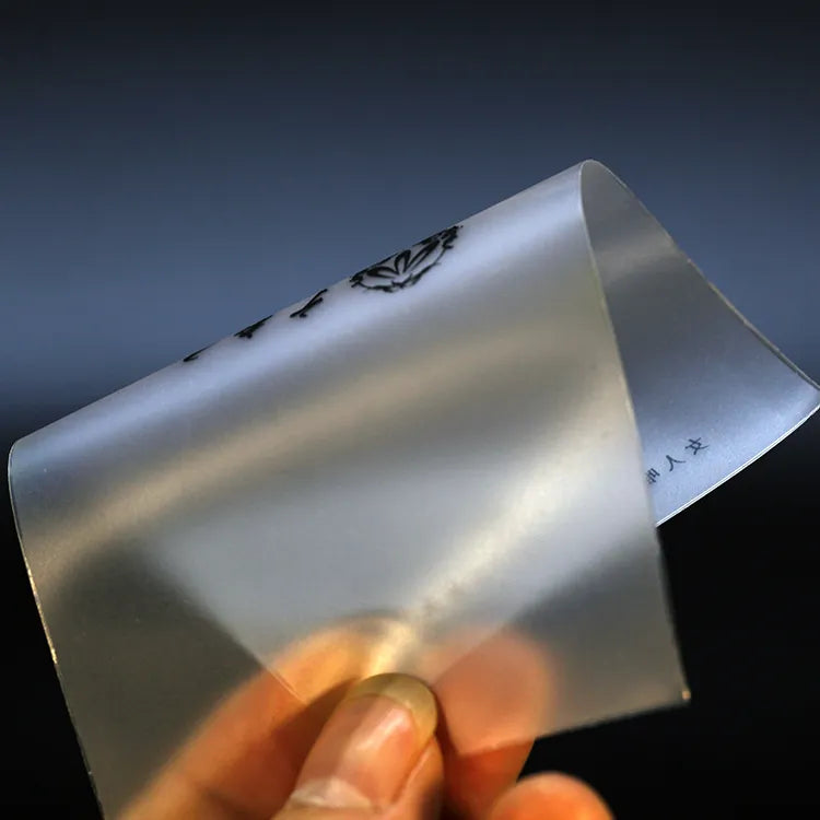 Hand holding a curved frosted translucent label strip with black printed text, showing its flexible surface