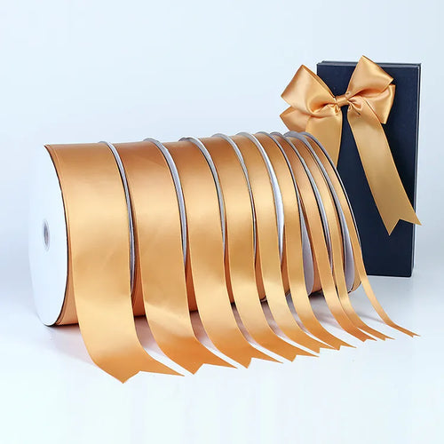 Gold satin ribbon spools in multiple widths arranged with a luxury black gift box and ribbon bow