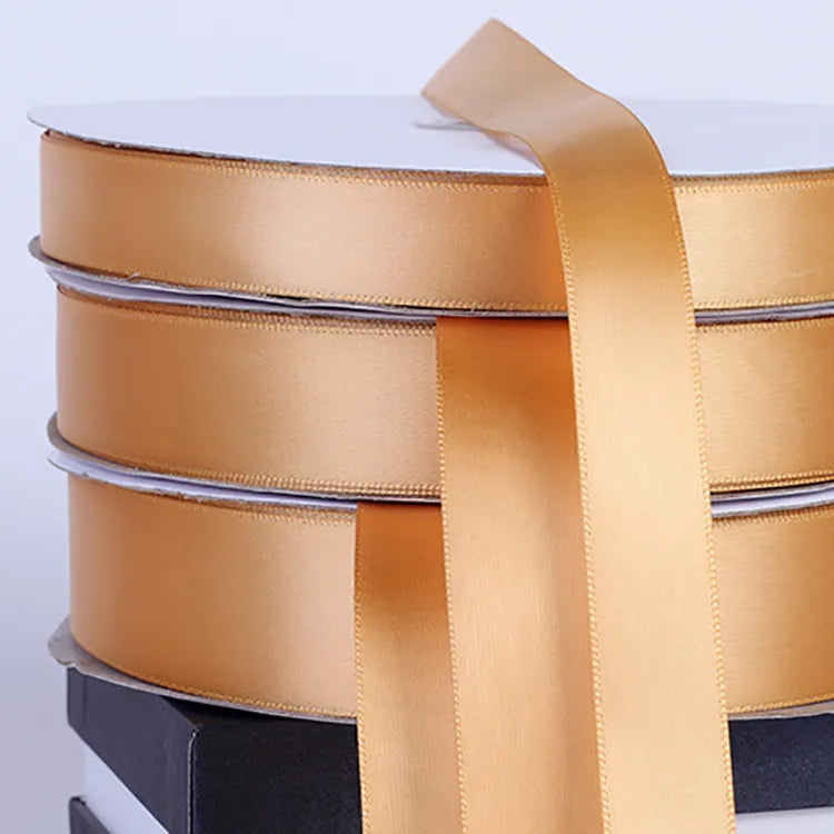 Close-up stack of wide gold satin ribbon spools displaying glossy finish and woven edges