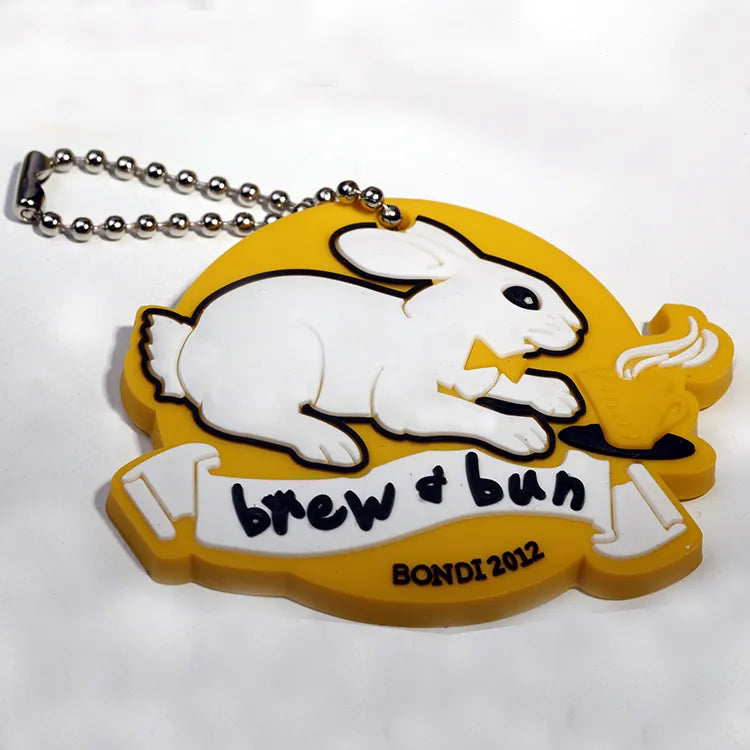 Custom yellow silicone rubber keychain pendant with a white rabbit design, raised lettering and ball chain