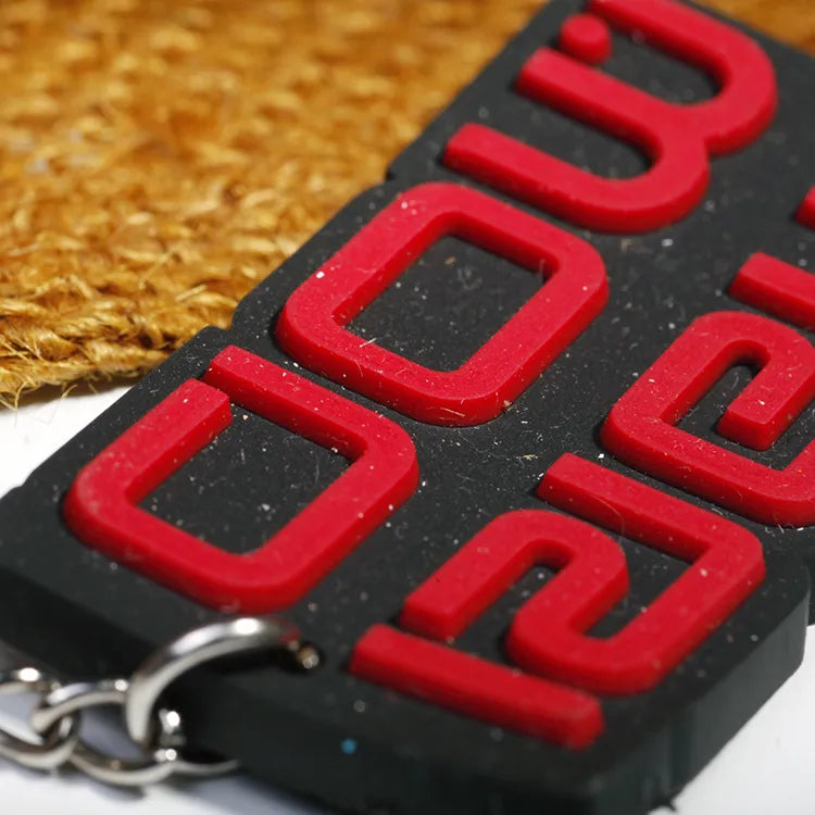 Close-up of red raised silicone lettering on a black PVC rubber keychain with metal ring