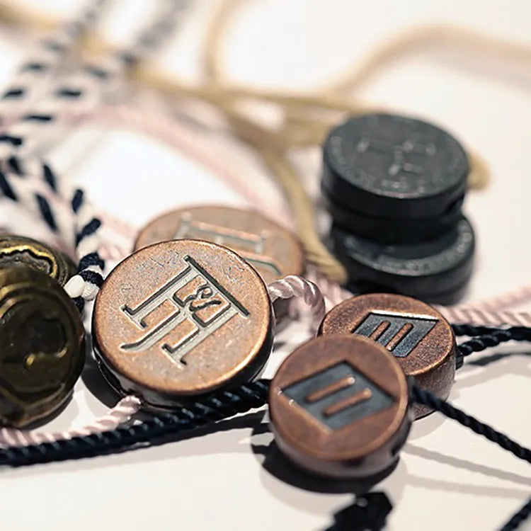 Assorted round seal tag buttons in copper, brass and black tones with twisted cords