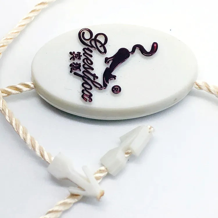 White oval plastic string tag with printed logo, cream twisted cord and white plastic barb fasteners