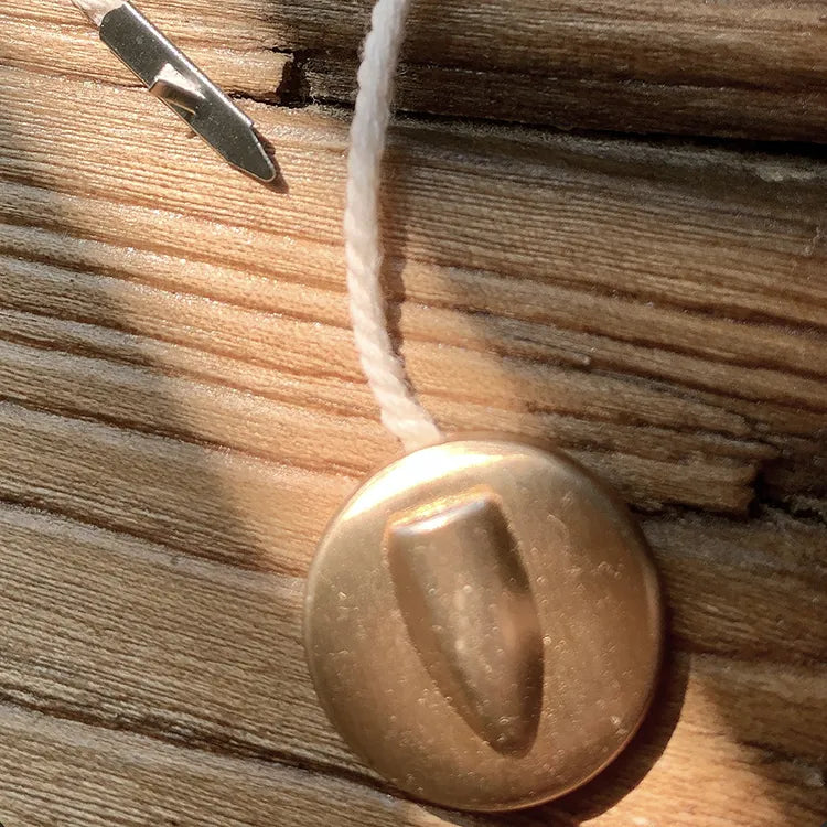 Round brass-tone button seal tag with white twisted cord and tagging needle
