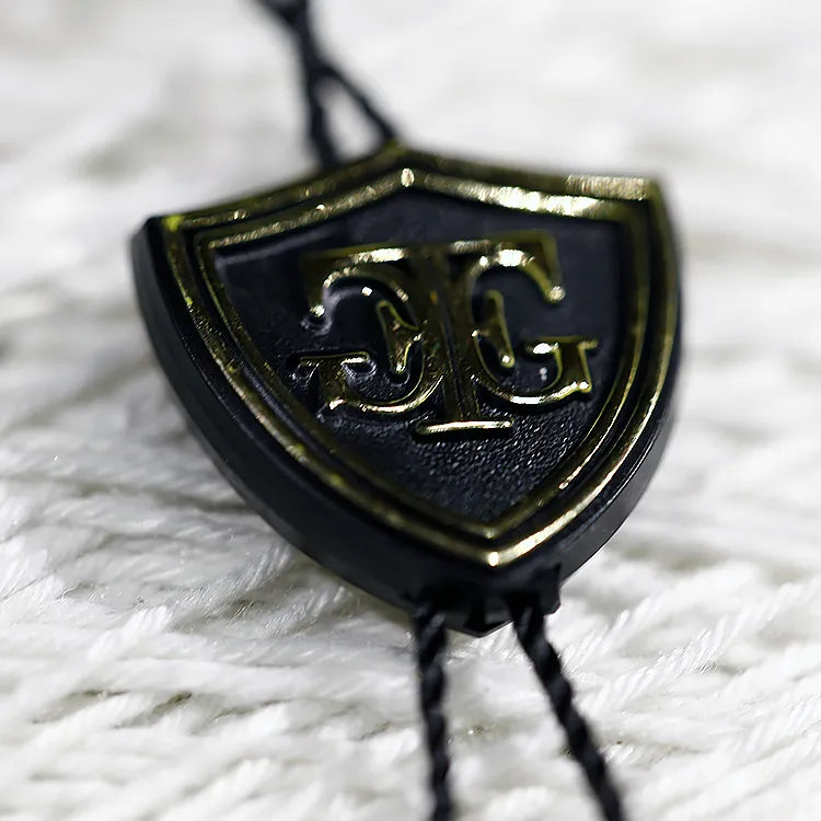 Black shield-shaped plastic string tag with gold emblem and black twisted cords