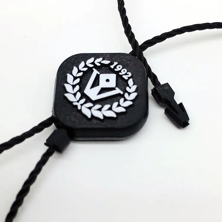 Black square plastic string tag with laurel emblem, black twisted cords and plastic barb fasteners
