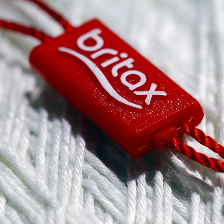 Red rectangular plastic string tag closeup with twisted red cord on white knit fabric