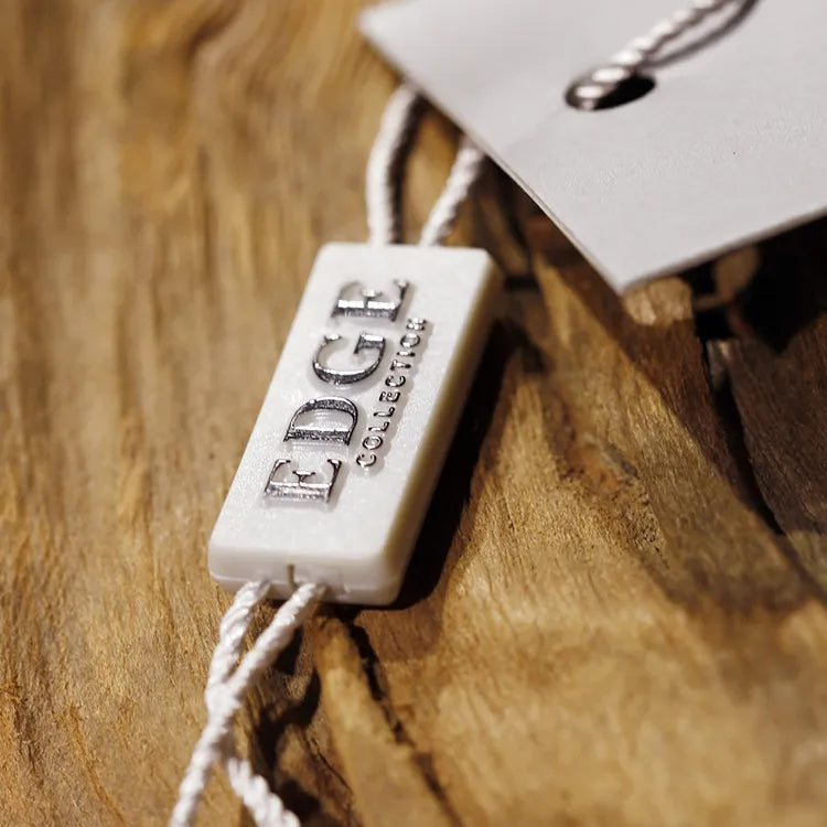 White rectangular plastic string tag with embossed lettering and white twisted cords threaded through a paper hang tag