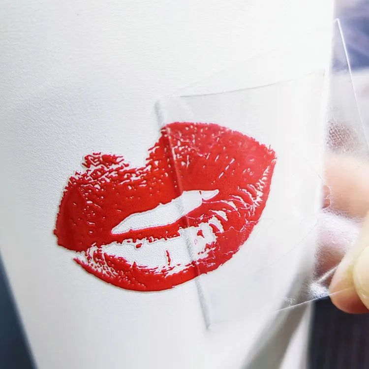 Red lip motif on a white surface with clear transfer film being removed