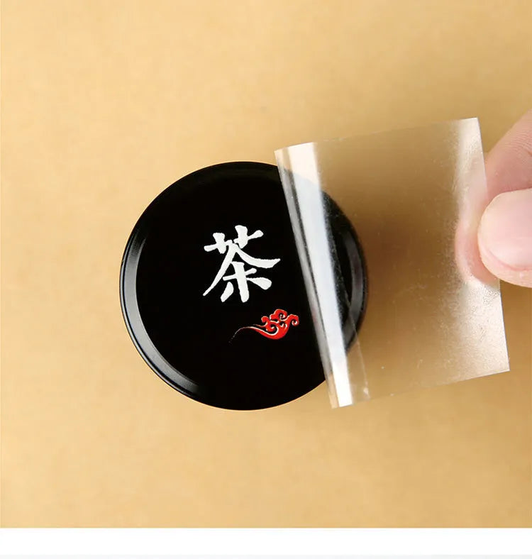 White character and red decorative detail transferred onto a black tea tin lid