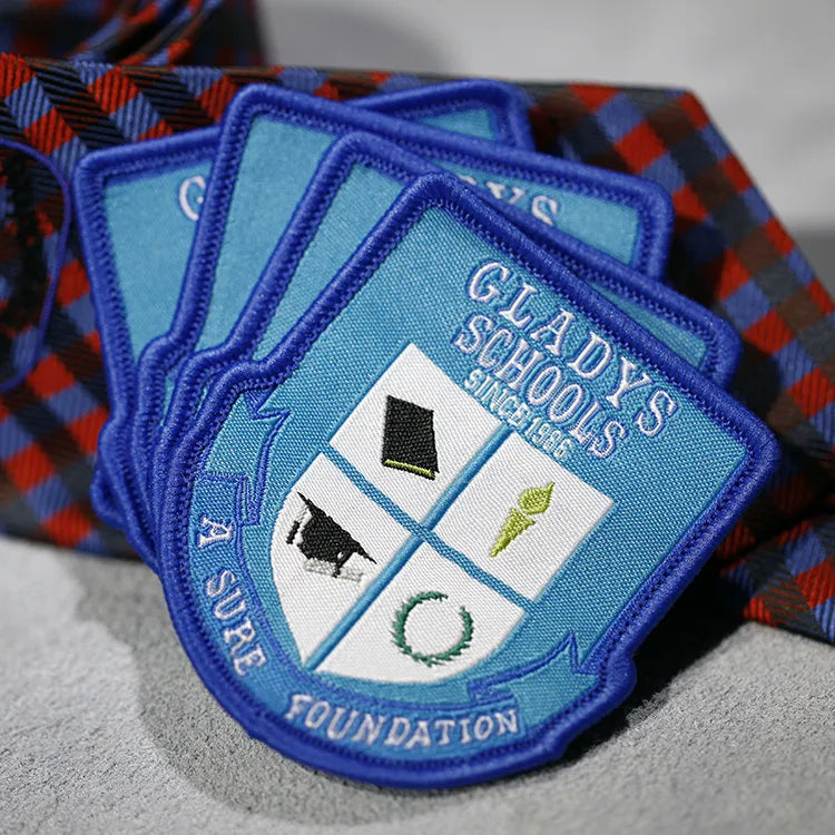 Blue shield-shaped woven school badges with white lettering and a quartered emblem