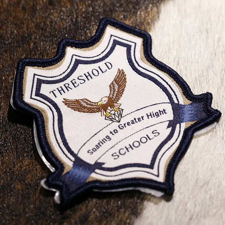 White shaped crest patch with dark outlines, lettering and a bird emblem