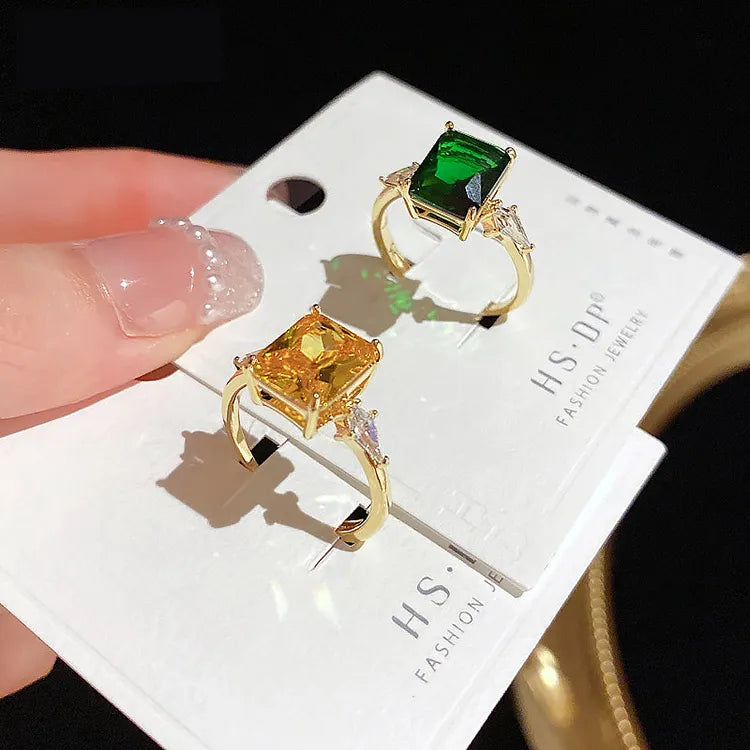 Close-up hand holding custom white jewelry display card mounting two luxury emerald-cut gemstone rings