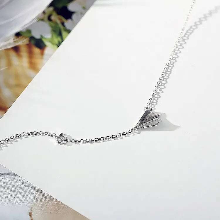 Silver airplane pendant chain laid across white presentation cardstock surface