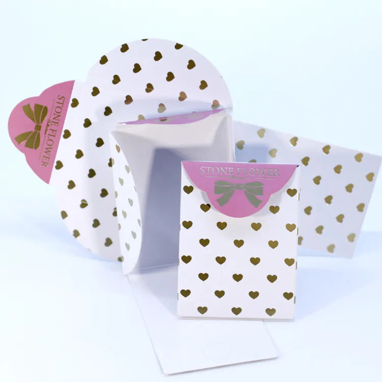 Close-up of foldable white cardstock jewelry gift packaging card with gold foil heart pattern