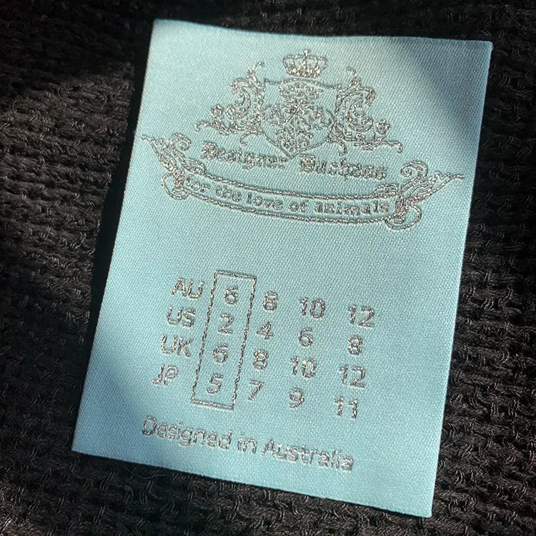 Light blue woven clothing label with ornate crest, size symbols, and “Designed in Australia” text