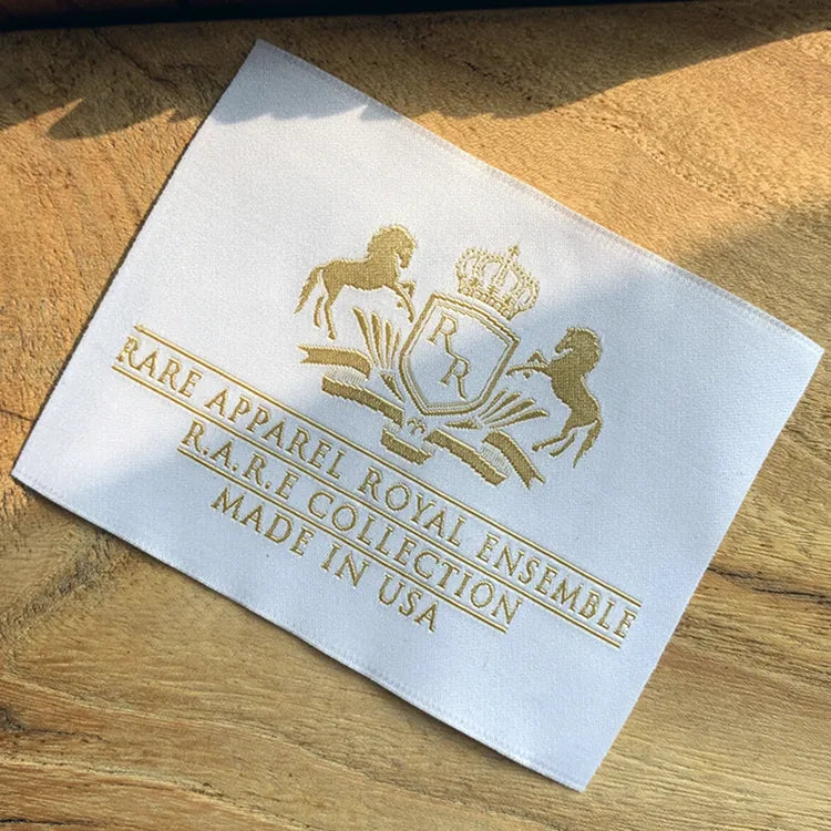 White woven clothing label with gold royal crest, “Rare Apparel Royal Ensemble & Collection,” Made in USA