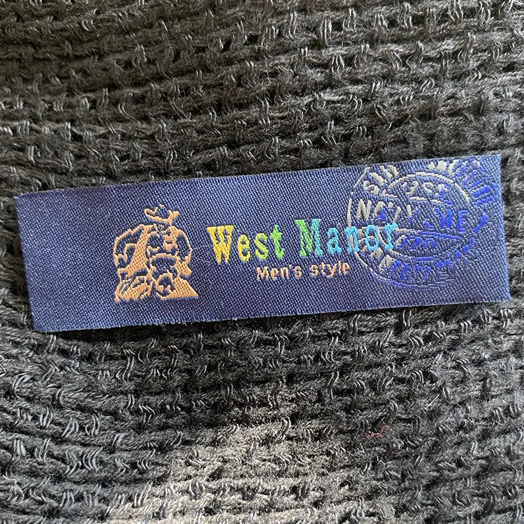 Dark blue woven clothing label with multicolored lettering, a gold crest and a blue circular emblem on black textured fabric