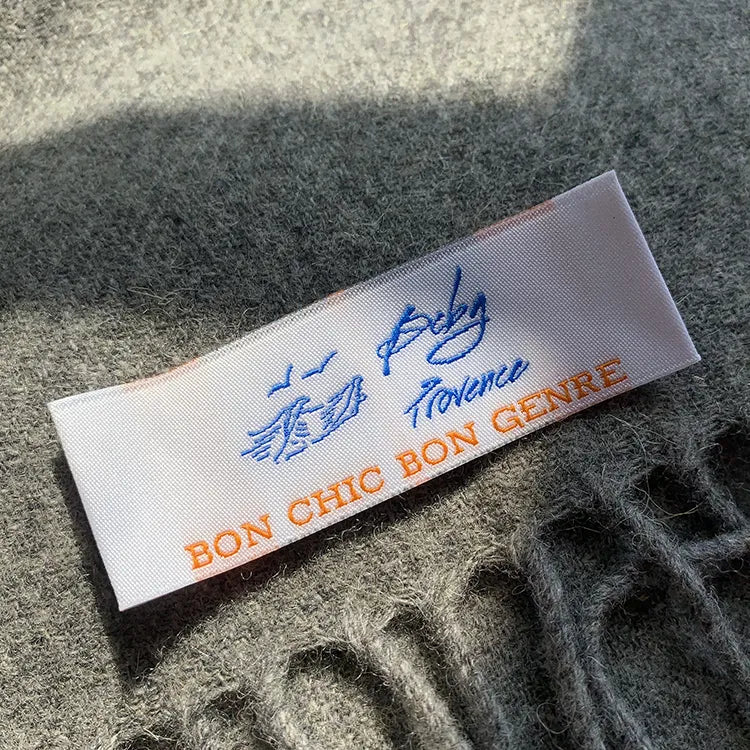 White woven clothing label with blue logo and orange lettering