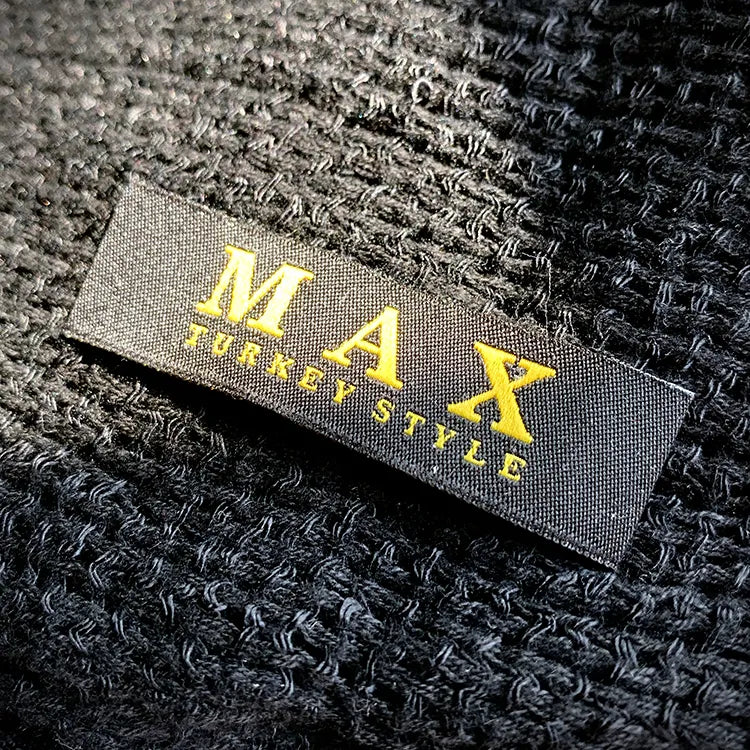Black woven clothing label with yellow MAX lettering on textured black fabric