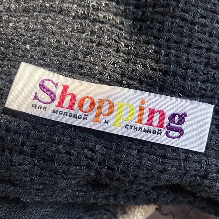 White woven clothing label with multicolored Shopping lettering on black textured fabric