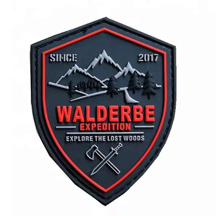Custom shield-shaped outdoor expedition PVC rubber patch with mountain, pine trees, and crossed axe emblem